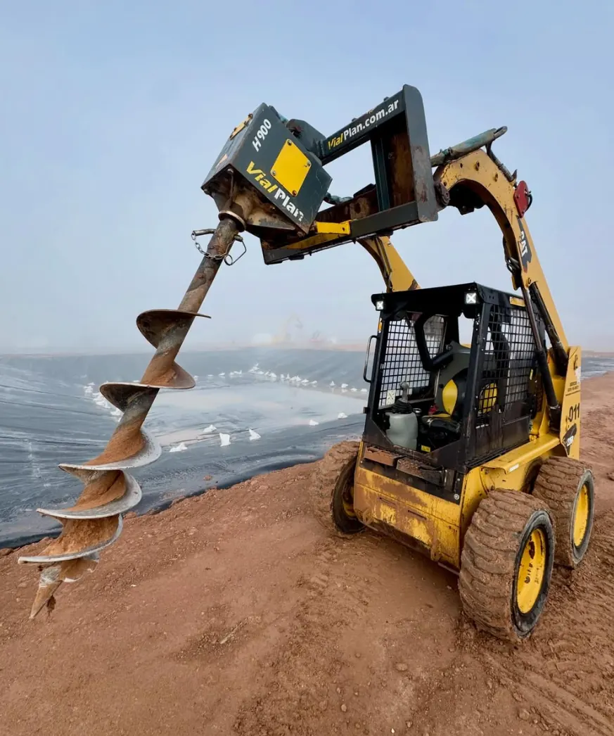 Minicargadora con hoyadora perforando el suelo
