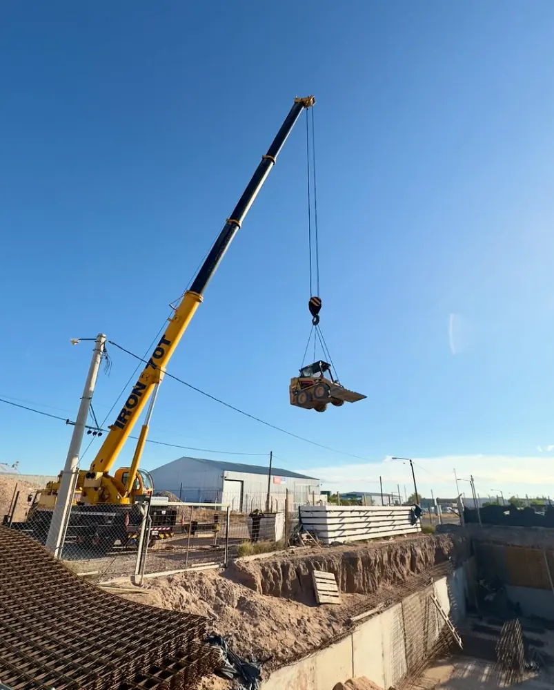 Grúa bajando la minicargadora a una excavación