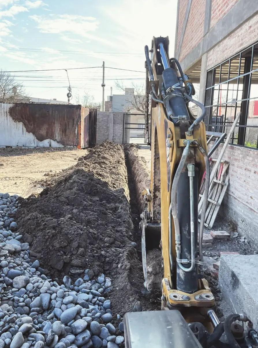 Retro con balde abriendo una zanja junto a una construcción